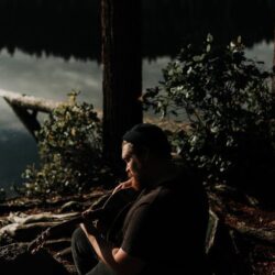 man playing guitar near trees and and body of water