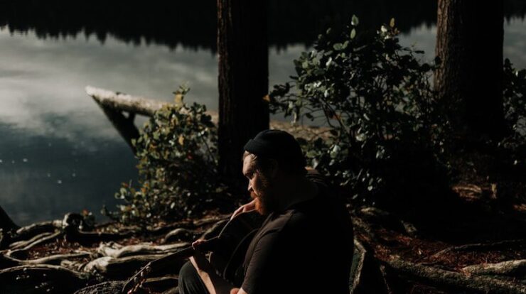 man playing guitar near trees and and body of water