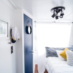 four pillows on quilted white bed near blue door and window with white curtain inside well-lighted room